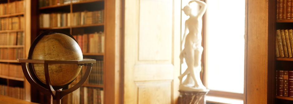 About the LLC 940x335 Image of a globe and a marble statue of a woman by a window in a library.
