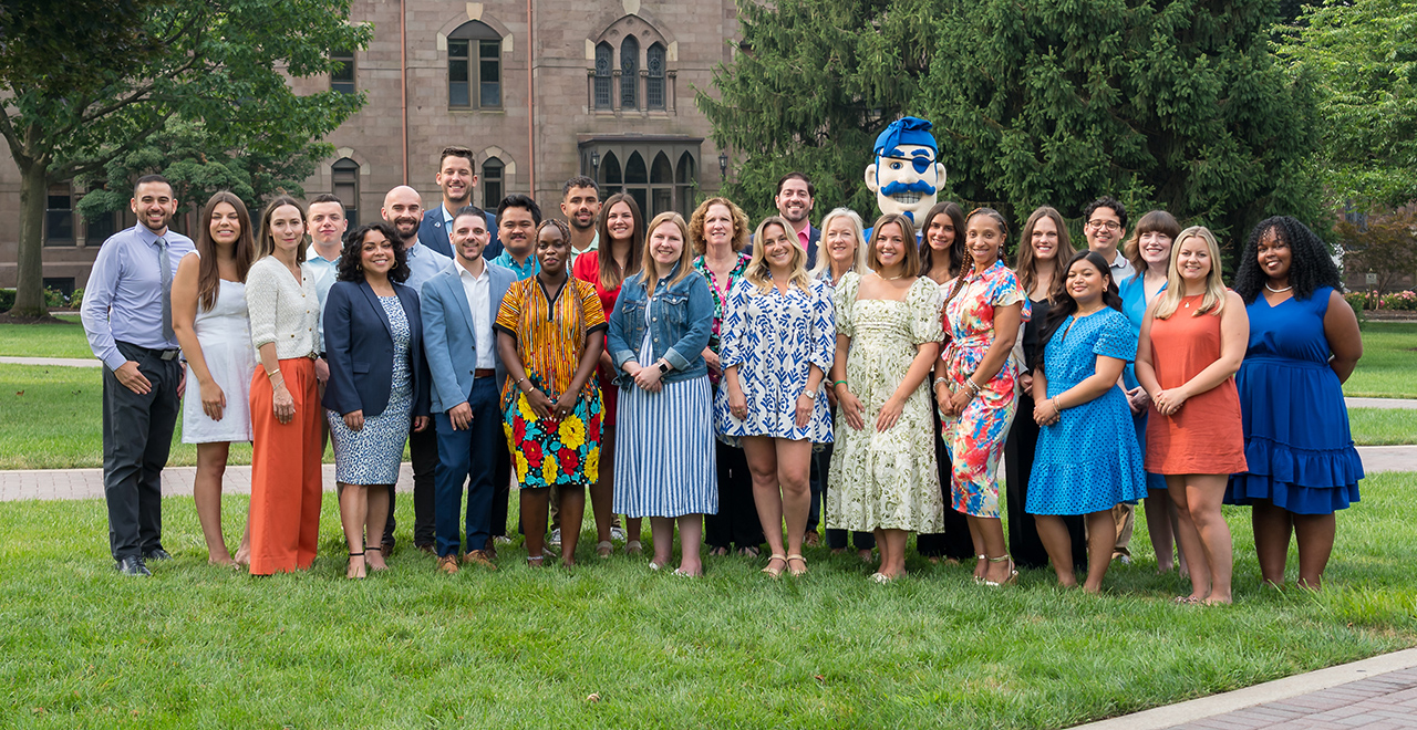 A photo of the admissions counselors team holding a Welcome to Seton Hall sign on the University Green.
