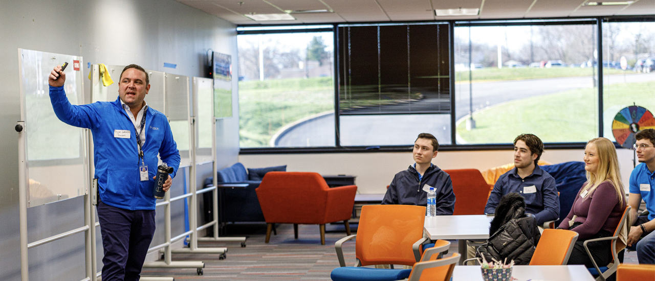 Image of students sitting and listening to a lecture as they are visiting Fusion Health, started by a Seton Hall alumni.