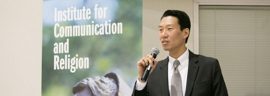 Ki Joo Choi speaking with a microphone at the inaugural event for the Institute of Communication and Religion.