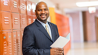 education leadership 320x180 Photo of person smiling, holding booklet in their hands in front of a locker