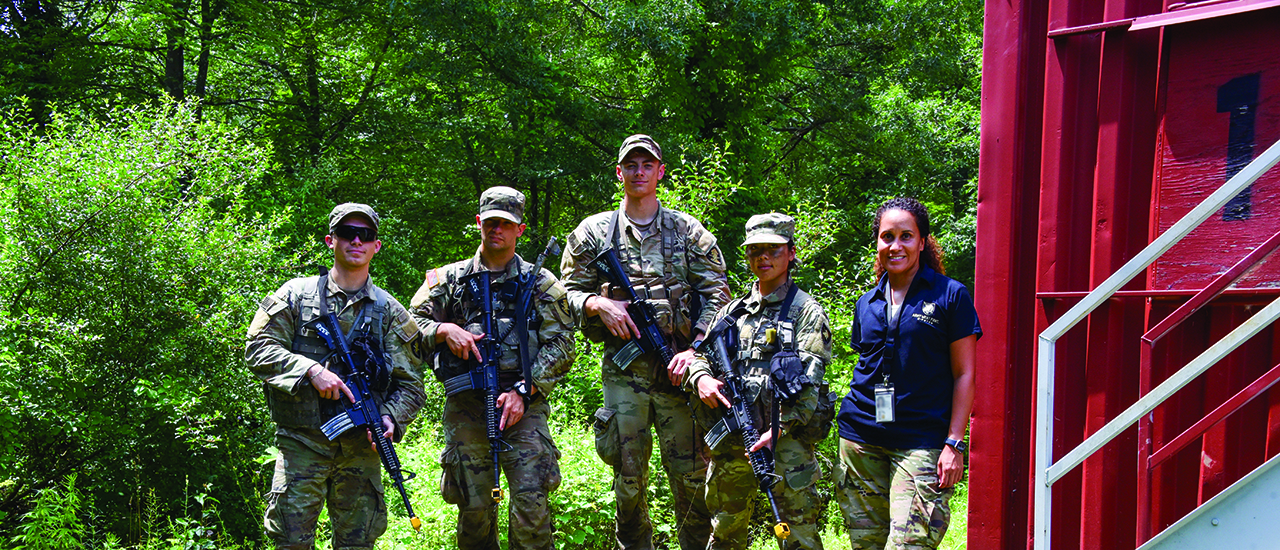 Beyond the Code - Photographs by Erika Norton Military personnel in the woods with a robotic dog.