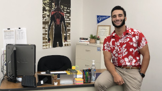 jameslopez320x180 James Lopez sitting on a desk and smiling