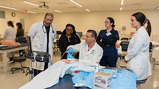 A group of nursing students surrounding an instructor and a mannakin.