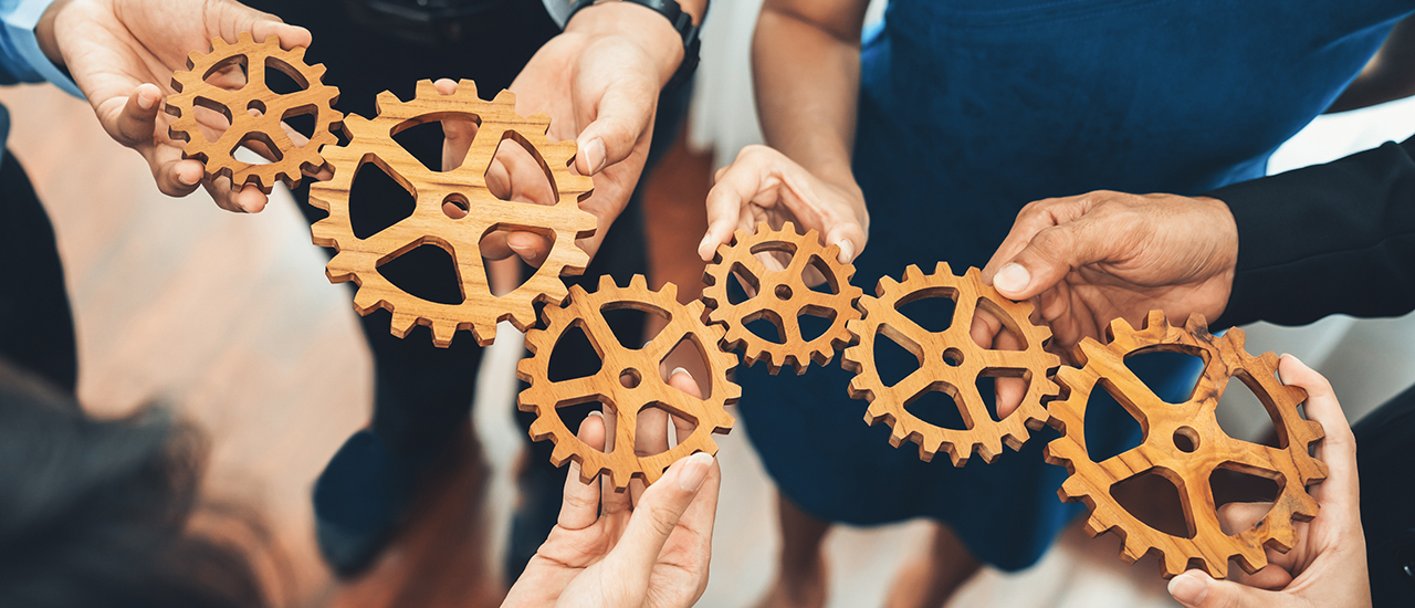 People holding gears working to fit them together. People holding gears working to fit them together.