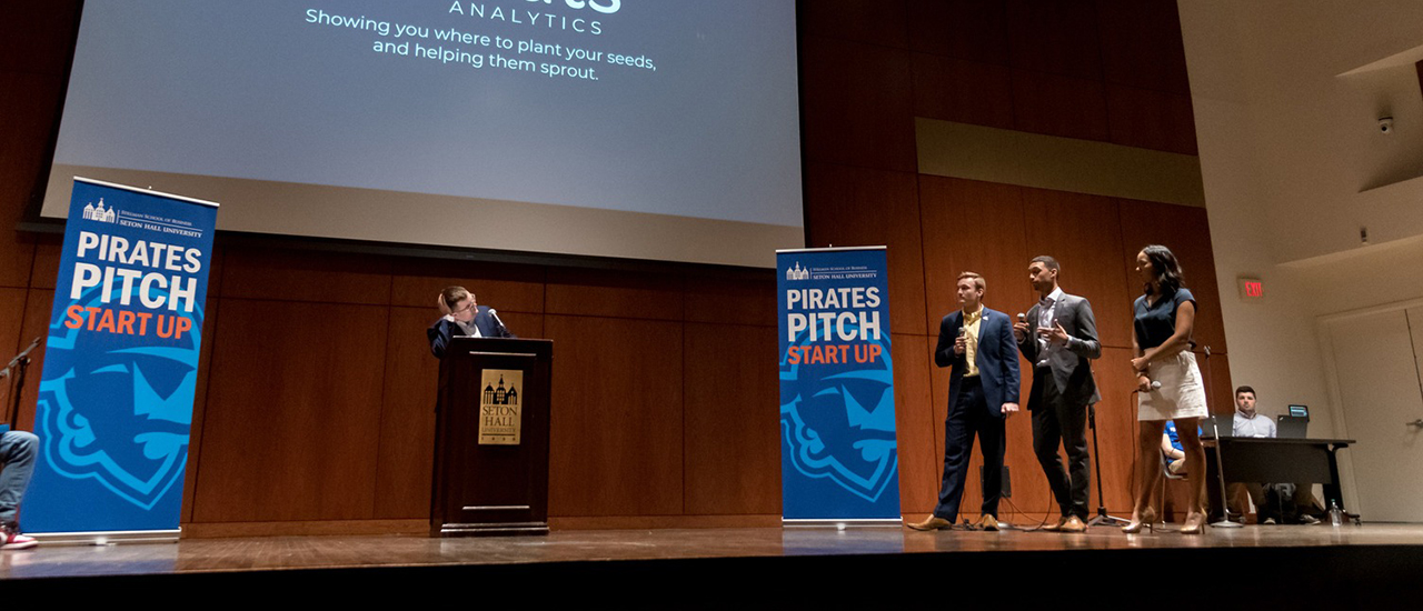 Pirates Pitch stage. Image of a participant at a podium and three judges during Pirates Pitch.