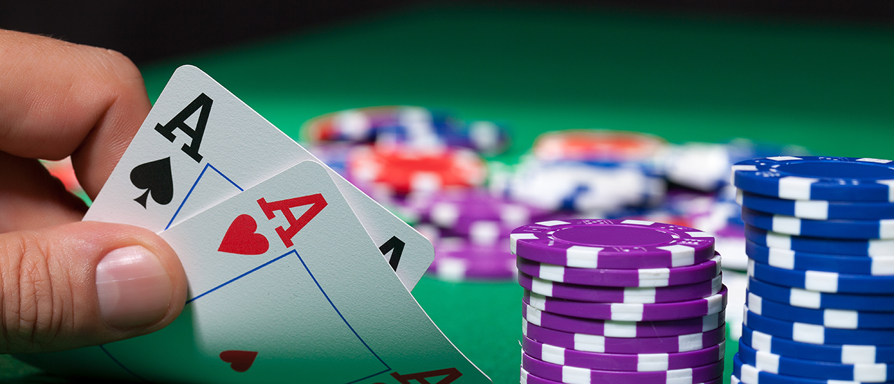 A Poker Hand A hand holding 2 aces over a poker table with piles of chips.